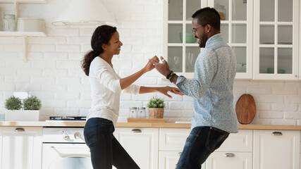 Smiling african american young couple dancing together in modern design kitchen, moving to new shared own house, happy loving biracial husband and wife have fun celebrate relocation, rental concept - Powered by Adobe