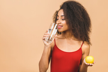 Dieting concept. Young African American woman isolated on beige background with an apple and with a glass of water.