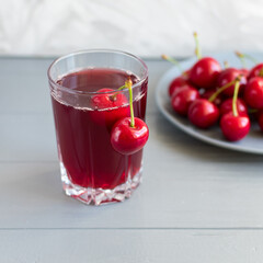 Cherry juice in a glass cup with cherry berries on a plate on a gray table. Selective focus.