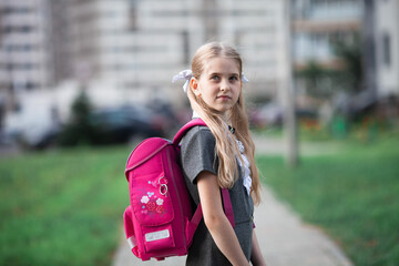 A schoolgirl wearing school uniform and carrying a big pink backpack goes to school. Back to school.