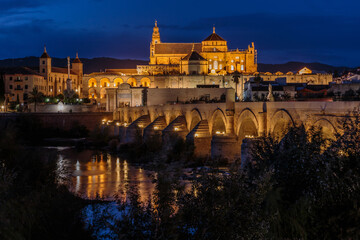 Fototapeta na wymiar Cordoba old town in the evening at the blue hour. Mosque Cathedral with Roman bridge and river course. Illuminated buildings of the Spanish city in Andalusia