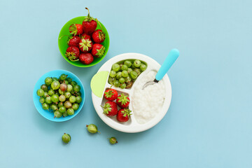 Plate with boiled rice and berries for child on color background