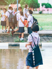 Female elementary school student wear face mask to prevent the Coronavirus(Covid-19) wait for her parents to pick her up to return home after school and the rain just stop in front of the school gate