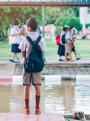 Male elementary school student wear face mask to prevent the Coronavirus(Covid-19) wait for her parents to pick her up to return home after school and the rain just stop in front of the school gate