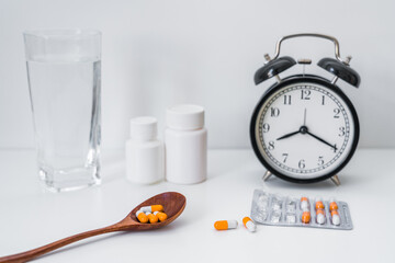 Capsules, alarm clock and a glass of water on the blue table-the concept of taking medicine on time