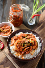 Stir fried kimchi with pork on cooked rice in a bowl with chopsticks on wooden background, Korean food