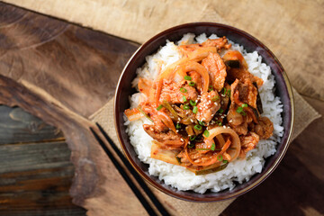 Stir fried kimchi with pork on cooked rice in a bowl on wooden background, Korean food