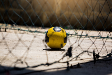 Yellow soccer ball with blurry mesh in soccer field. Classic soccer ball image with light shadow reflection and mesh around football field.
