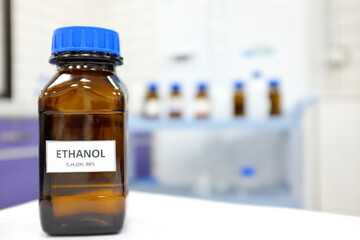 Selective focus of ethanol or ethyl alcohol brown amber glass bottle inside a laboratory. Blurred background with copy space. - obrazy, fototapety, plakaty
