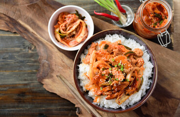 Stir fried kimchi with pork on cooked rice in a bowl on wooden background, Korean food