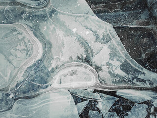 Close up abstract background of a frozen puddle. Cracked pothole ice texture, winter season pattern.