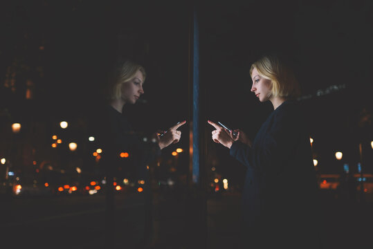 Caucasian young woman verifies account balance on banking application via modern kiosk with digital sensitive screen, charming female touching big digital display with reflected on her screen light