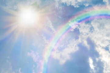 Summer sun burst and blue sky  rainbow - massive sun radiating beside fluffy clouds with a giant arcing rainbow and beautiful blue summer sky with copy space for messages
