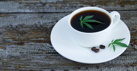 Cup of cannabis coffee with hemp leaves and roasted coffee beans on wooden table