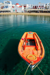 Fototapeta na wymiar Greek fishing boat in clear sea water in port of Mykonos. Chora town, Mykonos, Greece