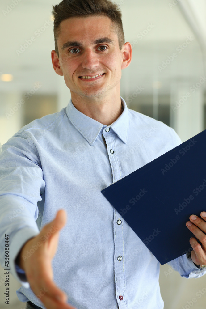 Wall mural waist up portrait of smiling male in shirt standing and holding folder while giving hand for greetin