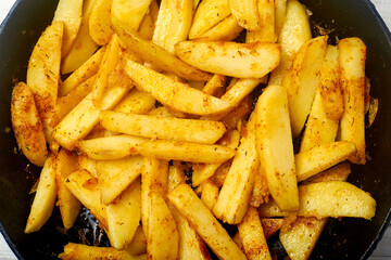 Sliced potato with spices. Cooking fried potatoes in a pan.