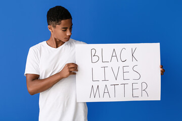 Sad African-American teenage boy with poster on color background. Stop racism