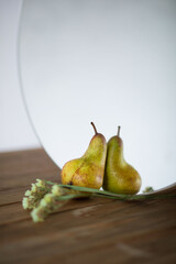Fresh ripe organic yellow pear stands on a rustic wooden table near a round mirror. Femininity. the concept of care. Selective focus. Space for text