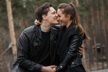 young couple in black jackets hugging and posing in the forest.