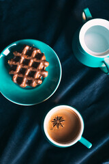 Top view of a coffee set, chocolate covered belgian waffle, velvet surface