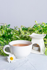 White cup of tea and aromalamp on the background of fresh wildflowers. Concept of rest, relaxation.