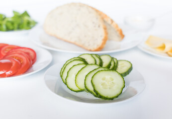 Ingredients for a healthy sandwich on white plates on a white surface. Tomato, cucumber and slices of bread