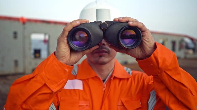 Filipino deck Officer on deck of vessel or ship , wearing PPE personal protective equipment. He is looking through binoculars.