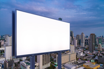 Fototapeta premium Blank white road billboard with Bangkok cityscape background at night time. Street advertising poster, mock up, 3D rendering. Side view. The concept of marketing communication to sell idea.