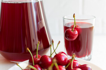 Cherry juice in a glass cup with cherry berries on a plate on a gray table. Selective focus.