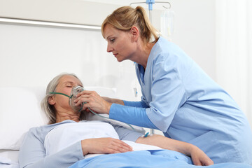 Fototapeta premium nurse puts oxygen mask on elderly woman patient lying in the hospital room bed