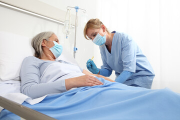 Fototapeta premium nurse with the syringe injects the vaccine to the elderly woman patient lying in the hospital room bed, wearing protective gloves and medical surgical mask, coronavirus covid 19 protection concept