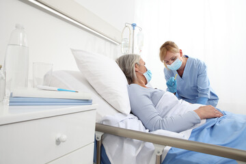 nurse with the syringe injects the vaccine to the elderly woman patient lying in the hospital room...