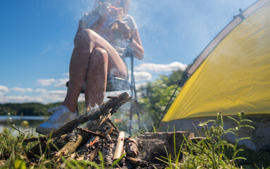 Woman is eating instant noodles next to tent by the lake.