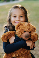 Cute Girl Smile Embrace Toy Teddy Bear Outdoors. Attractive Caucasian Female Child Hug Children Stuffed Animal Closeup. Happy Kid Enjoy Positive Emotions Vertical Position Bach-to-school Concept