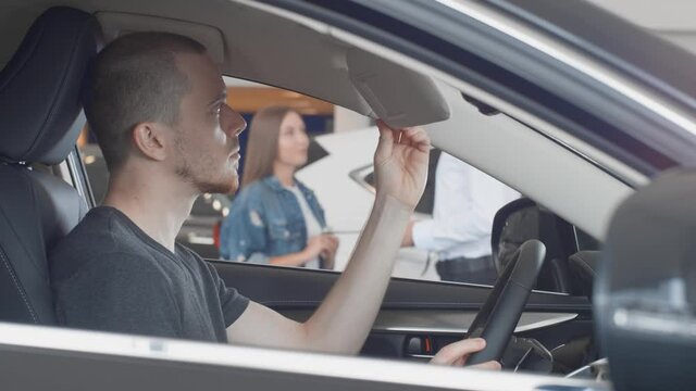 a married couple choose a new car at a car dealership, a young man looks at the car interior