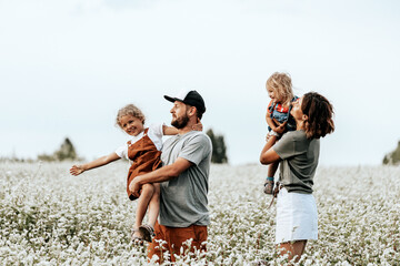Happy family is playing, having fun on the field with flowers at sunset. Family and love concept. Young family housing concept