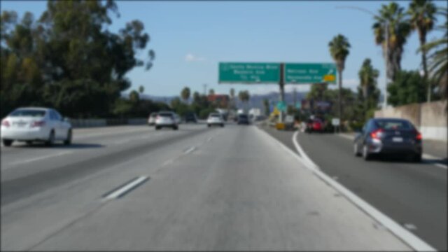 Driving on intercity freeway in Los Angeles, California USA. Defocused view from car thru glass windshield on busy interstate highway. Blurred suburb multiple lane driveway. Camera inside auto in LA.
