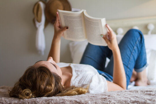 Chica tumbada en la cama leyendo un libro en su habitación