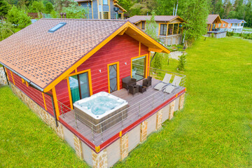 Cottage village top view. House with bathtub for spa treatments. Hot tub is located on balcony. Concept - rental of suburban real estate. Exterior of a country cottage. Concept - sale of home pools.