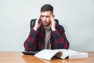 Man is upset. Concept - headache from reading. Concept - fatigue at work. Man is counting expenses. Big contract and calculator on table. Guy holds his head. Man has stress due to financial situation