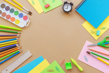 School supplies stationery, colour pencils, paints, alarm clock, paper on beige background. Back to school concept