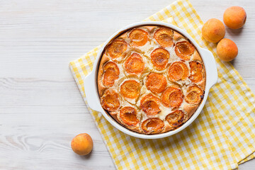 homemade apricot pie in a white form on a light wooden background with cup of tea, delicious pastries, summer dessert