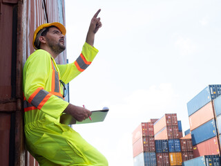 Smart engineer man wearing safety helmet doing stock tick check and cardboard stock container management in container yard background..