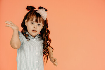 Surprised girl with Down syndrome in a dress, pink background in the background. Happy baby...