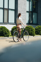 selective focus of businesswoman walking with bicycle near modern building