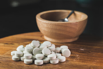Fototapeta na wymiar Pile of white pills on a wooden surface, wooden bowl and silver spoon