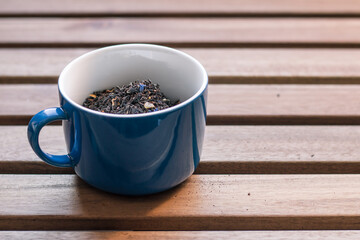 Blue cup filled with dried tea leaves on a wooden table