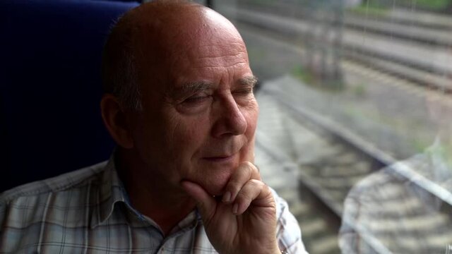 Close up portrait of an elderly man sad rides on public transport and looks out the window of the outgoing road.