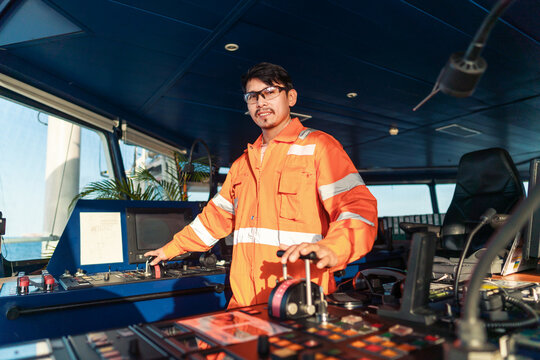 Filipino deck Officer on bridge of vessel or ship wearing coverall during navigaton watch at sea . He is maneuvering with cpp thrusters propulsion